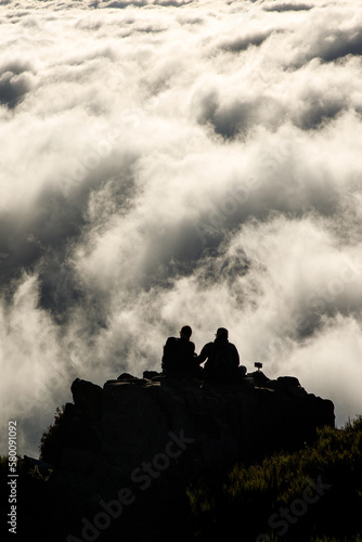 Two people on top of a mountain above the clouds