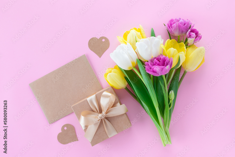 Bouquet of spring tulip flowers, gift and greeting card on pastel pink table for Mothers day. Flat lay.