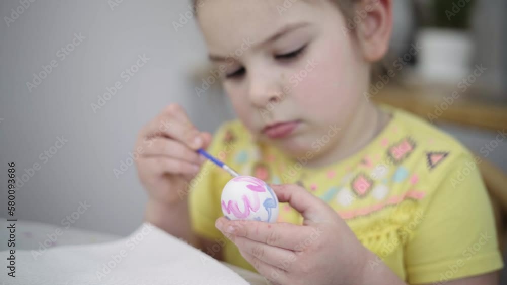Child girl of preschool age painting Easter eggs at home kitchen. Easter spring traditions. Slow motion Child girl of preschool age painting Easter eggs at home kitchen. Easter spring traditions. Slow motion