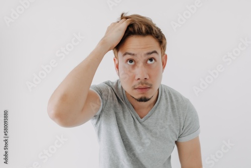 Asian man in grey t-shirt looking at his dyed hair doubtfully isolated on white. photo