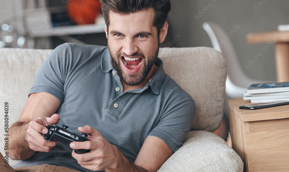Excited young handsome man playing video game a while sitting on the couch at home Excited young handsome man playing video game a while sitting on the couch at home