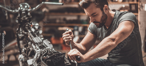 Canvas Print Confident young man repairing motorcycle in repair shop