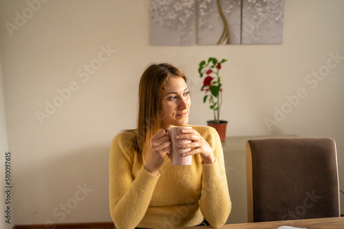 Young woman sitting in living room and drinking hot tea. 