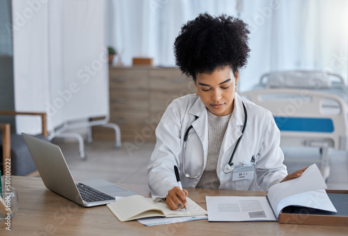 Black woman, laptop and doctor writing in notebook for healthcare test, study or research at the hospital. African American female medical expert taking notes in book for insurance, report or results photo