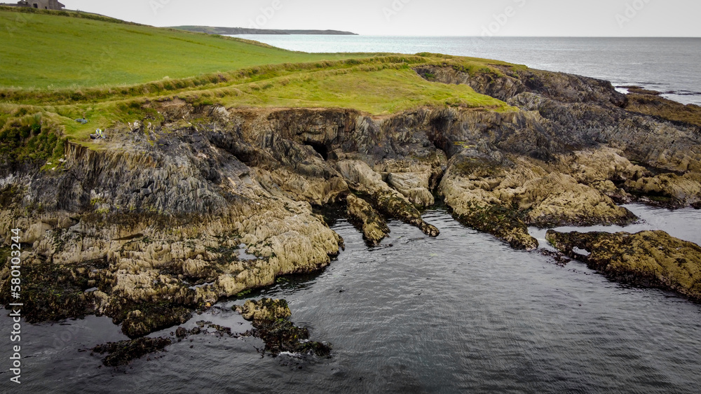 A picturesque rocky cape on the Atlantic coast of Ireland. Seaside landscape. Green grass field beside body of water