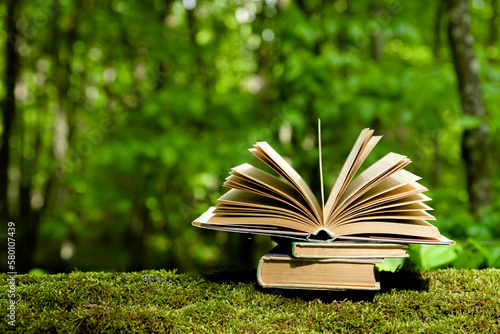 Old books lying on green moss in forest with trees in background. Open book with old paper pages. Concept of knowledge, wisdom, fairy tales