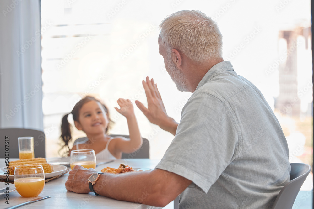 Obraz premium High five, breakfast and family with a girl and grandfather sitting at a dining room table for eating food. Motivation, health and children with a senior man encouraging his grandchild to eat healthy