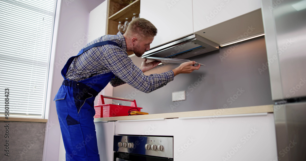 Young Handyman In Overall Fixing Kitchen Extractor Fan