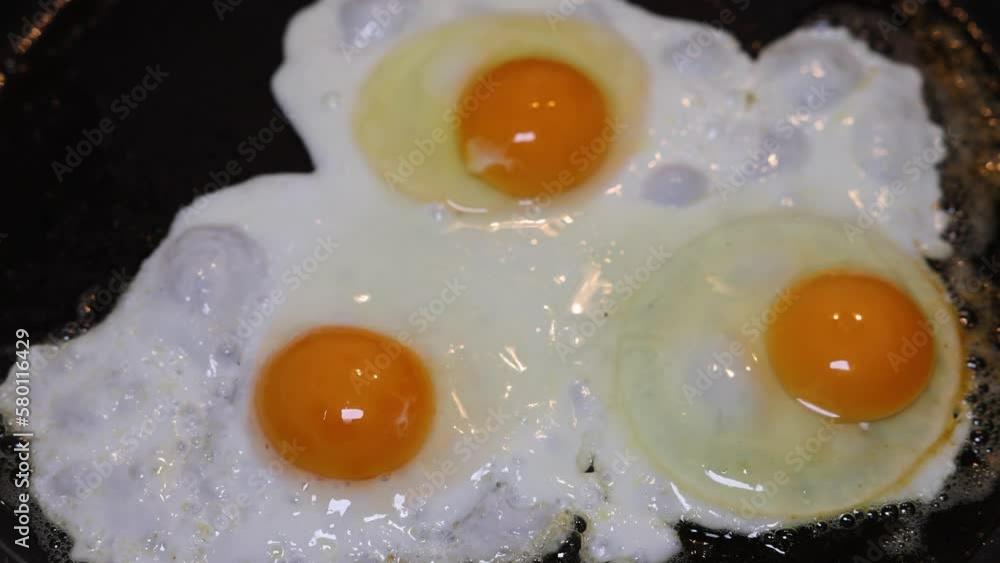 A chef fries three fried eggs in a black pan and serves them on the plate. A chef fries three fried eggs in a black pan and serves them on the plate.