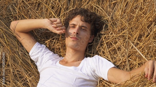 model man on a haystack with a straw in his hands