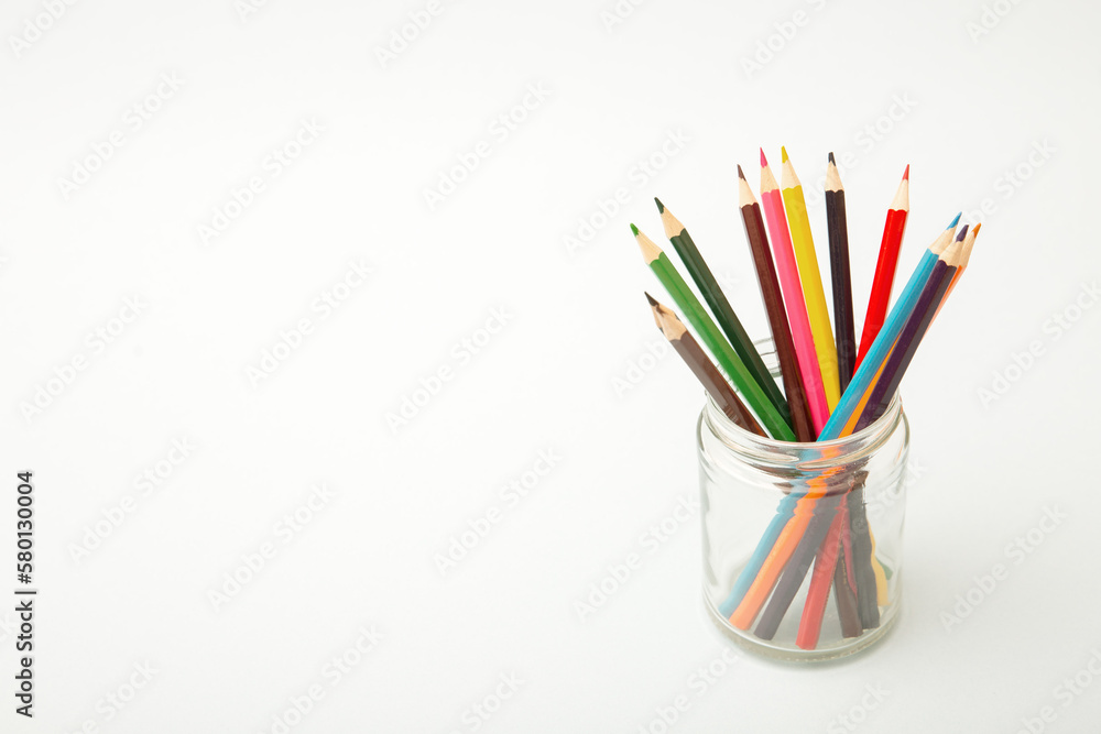 Multi-colored pencils in a glass jar on a white background. Copy space