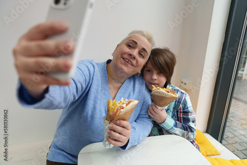 Mother takes a selfie with a smart phone while eating gyros in Greek restaurant. Happy family enjoying fast food lunch on the weekend