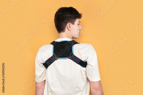 A young guy has a stooped back and bad posture, so he often wears a special bandage to support the back muscles, align the posture, medical concept photo