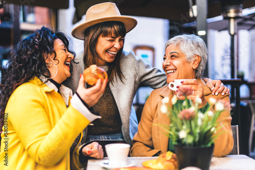 Happy three senior women enjoying breakfast eating croissant and drinking coffee at city bar cafeteria, Life style and Friendship concept with mature female people having fun outdoors sitting at table