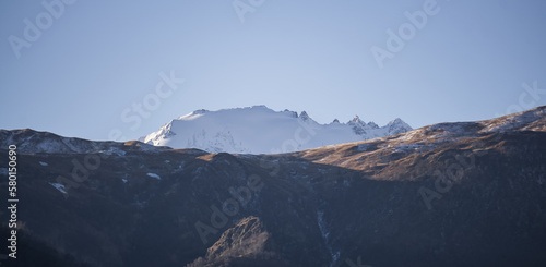 Panorama of mountain slopes with vegetation and trees yellowed in autumn and a rocky massif with snow, early autumn morning