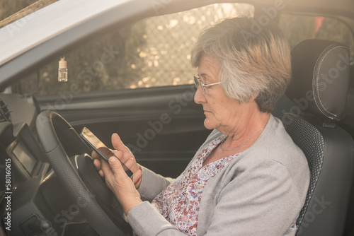 Senior woman with glasses inside her car looking at her mobile phone