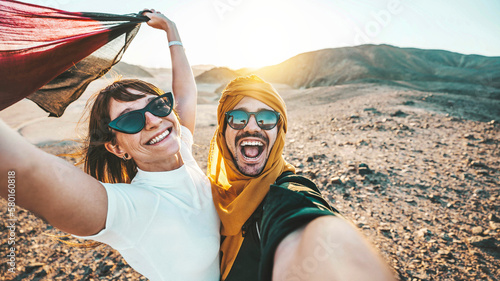 Happy couple of travelers taking selfie picture in rocky desert - Young man and woman having fun on summer vacation - Two friends enjoying summertime moment - Life style and travel concept.