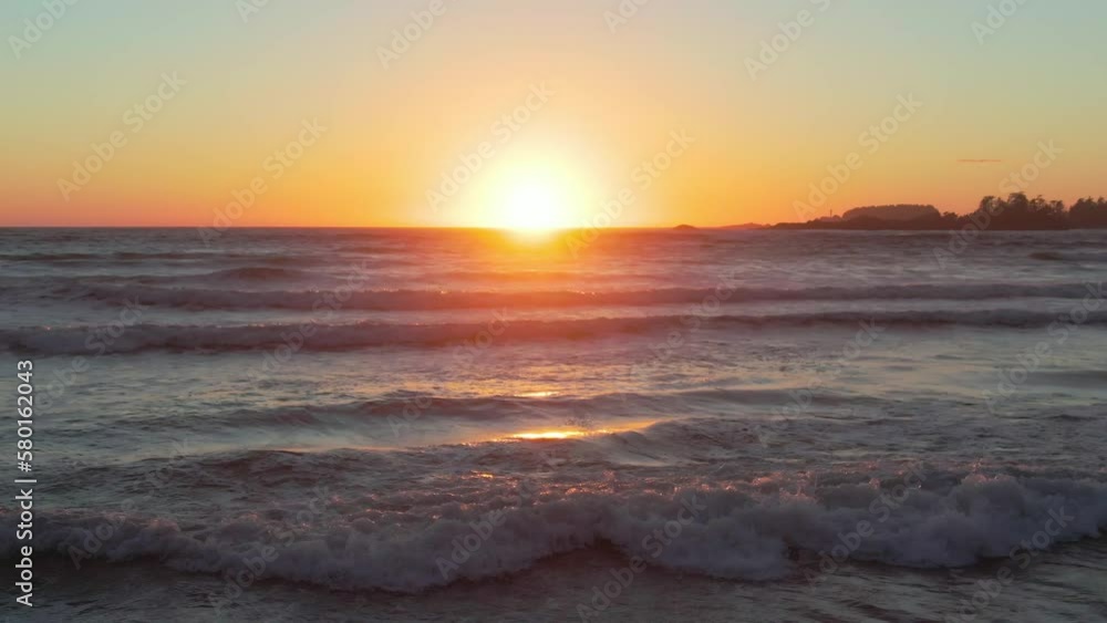 A drone shot over Chesterman beach at sunset with water waves moving around, sun shining background A drone shot over Chesterman beach at sunset with water waves moving around, sun shining background