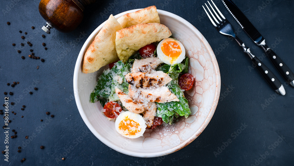 Caesar salad with chicken, parmesan cheese, lettuce, tomatoes, cut tortilla on a dark table. Caesar salad with chicken, parmesan cheese, lettuce, tomatoes, cut tortilla on a dark table.