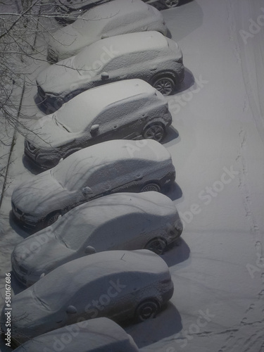 Night urban scene of the city life in winter time in snow storm, snowcovered cars parked on a road