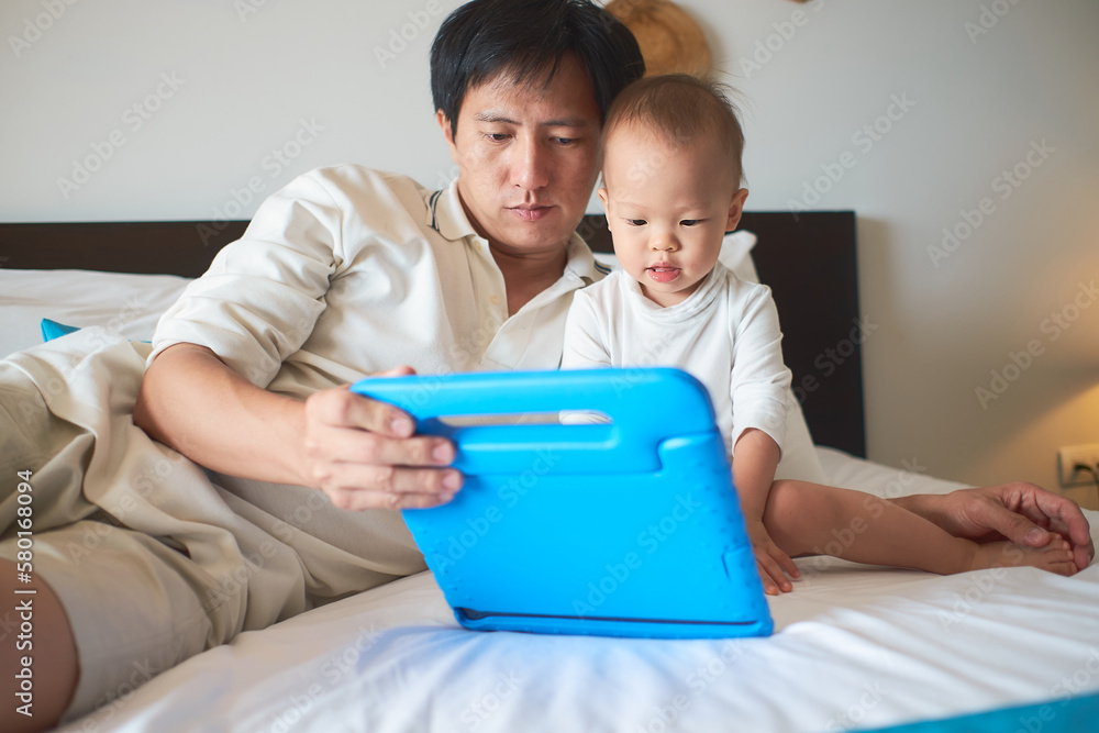 Father and son are using tablet while spending time together before go to bed at home, Dad and Cute little Asian 1 year old toddler baby boy child sitting on bed in bedroom, internet addiction concept Father and son are using tablet while spending time together before go to bed at home, Dad and Cute little Asian 1 year old toddler baby boy child sitting on bed in bedroom, internet addiction concept