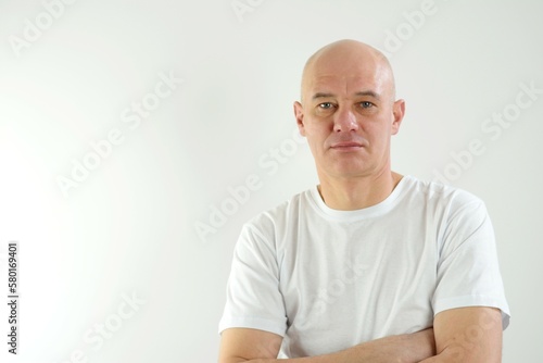 bald man wearing casual white t shirt with hand on chin thinking about question, pensive expression. smiling and thoughtful face. doubt concept. adult bald man put his hands on chest