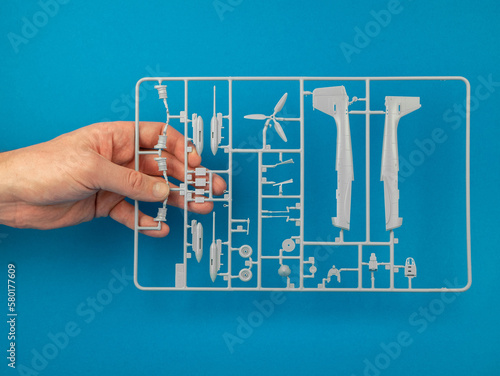 Sprue from a plastic model kit in hand on the blue background. Parts tree of the airplane model. Building model aircraft, hobby concept