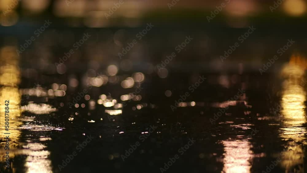 Atmospheric video of rainstorm in a night city. Heavy rain and splashes puddles taken from low point. Large drops break on the pavement in the light of street lamps. Slow motion Atmospheric video of rainstorm in a night city. Heavy rain and splashes puddles taken from low point. Large drops break on the pavement in the light of street lamps. Slow motion