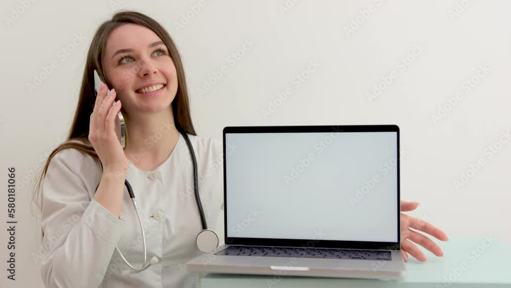 young doctor after institute practice at university in hospital talking on phone advertises new product on computer with white screen laptop in foreground in hands of phone woman laughing girl smiling young doctor after institute practice at university in hospital talking on phone advertises new product on computer with white screen laptop in foreground in hands of phone woman laughing girl smiling