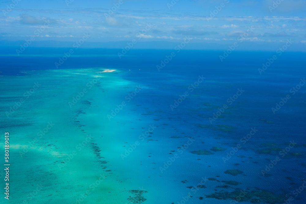 An aerial view of the coral reefs and clear turquoise waters surrounding Vlasoff Cay, a small white sand bar in the Great Barrier Reef — Coral Sea, Cairns; Far North Queensland, Australia