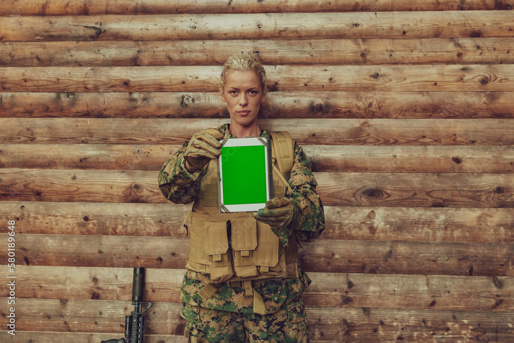 Woman soldier using tablet computer against old wooden wall in camp