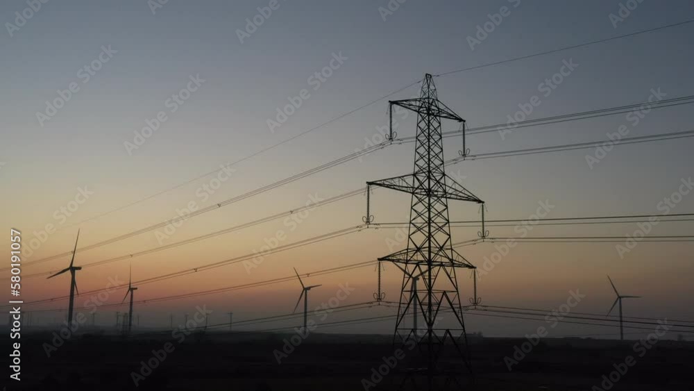 Wind turbines in the evening sunset as green technology powers electricity along power lines and pylons. Global warming in Manchester England UK 4K Wind turbines in the evening sunset as green technology powers electricity along power lines and pylons. Global warming in Manchester England UK 4K