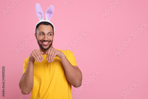 Happy African American man in bunny ears headband on pink background, space for text