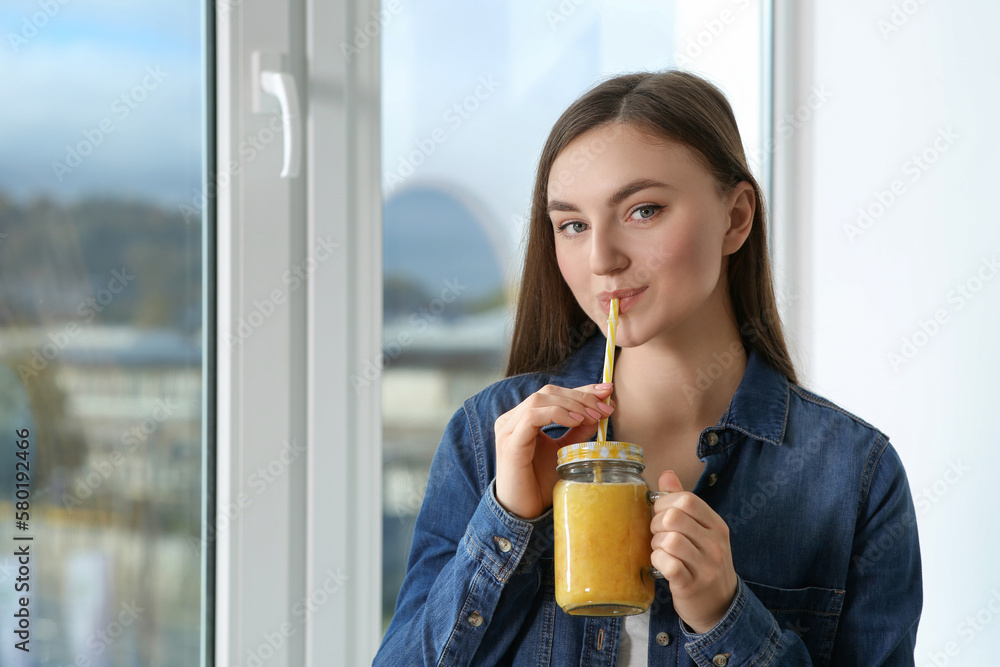 Beautiful young woman drinking delicious smoothie near window. Space for text Beautiful young woman drinking delicious smoothie near window. Space for text