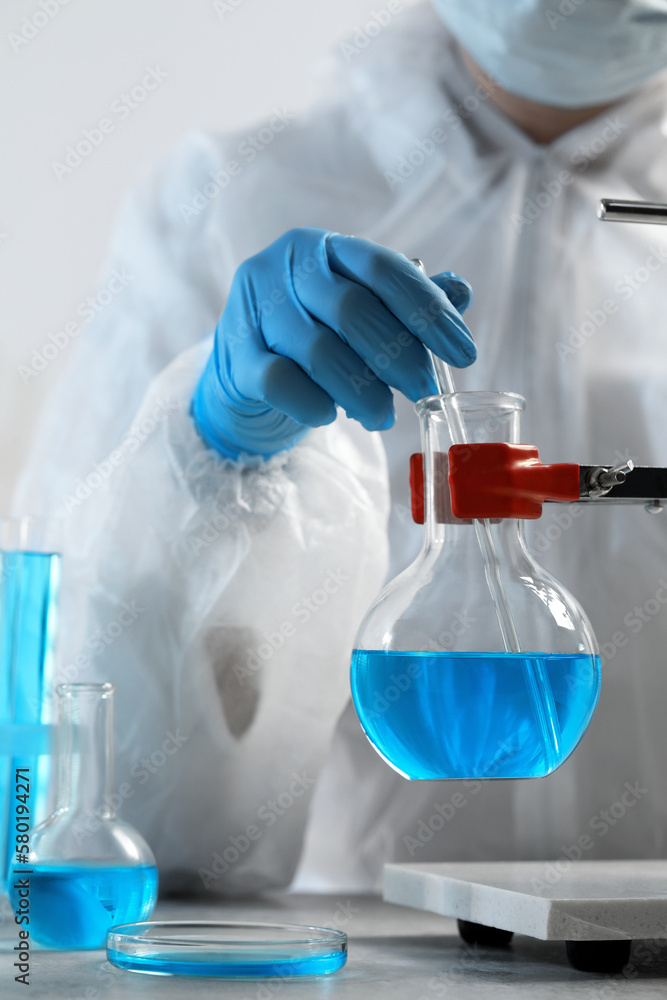 Scientist taking sample of light blue liquid in laboratory, closeup Scientist taking sample of light blue liquid in laboratory, closeup