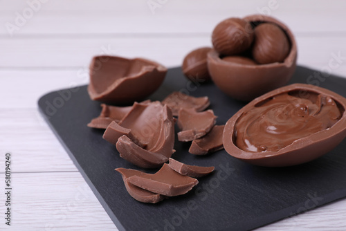 Broken and whole chocolate eggs with paste on white wooden table, closeup