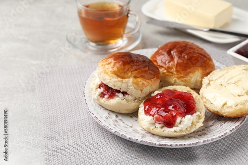 Freshly baked soda water scones with cranberry jam, butter and cup of tea on light grey mat. Space for text