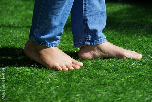 The feet of a woman wearing jeans step on the grass