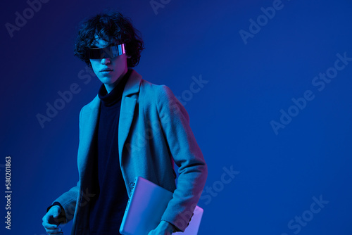 A man with a laptop in his hands and a jacket, futuristic glasses in blue light, Blue Perennial color, cyber security, technology, laptop copy space, template, trendy neon, freelance work, hacker