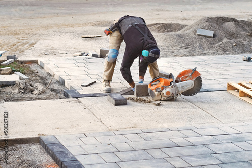 Landscape worker cutting and laying paving stones on residential driveway of a landscaping interlock construction site. Home renovation and improvement work business industry background.
