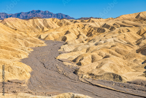 Wide view of remote desert mountains and rolling hills cut by a dry rocky stream bed on a clear day.