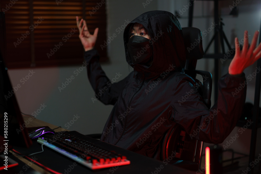 Hacker in hoodie raising hands while having problem with hacking programming system or server Hacker in hoodie raising hands while having problem with hacking programming system or server