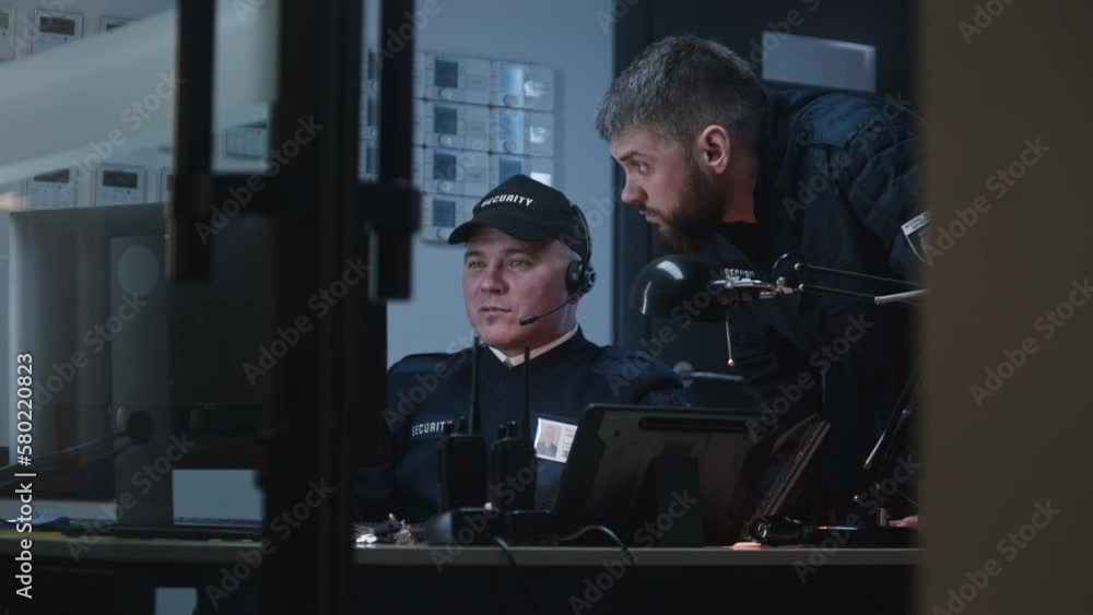 Two security officers talk and look view from security cameras displayed on computer monitors. Walkie talkie and surveillance equipment. Observation and CCTV technology. Monitoring and social safety. Two security officers talk and look view from security cameras displayed on computer monitors. Walkie talkie and surveillance equipment. Observation and CCTV technology. Monitoring and social safety.