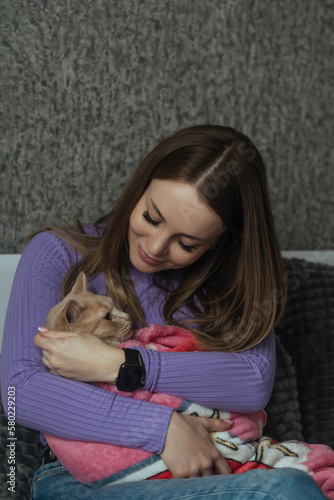 A young woman in her bedroom holds her pet cat wrapped in a baby blanket in her arms. Love and care for animals  childless woman. Treating animals like your children
