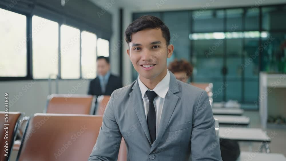 Close up smiling face of young Asian businessman wearing suit sitting at airport terminal looking at camera Close up smiling face of young Asian businessman wearing suit sitting at airport terminal looking at camera