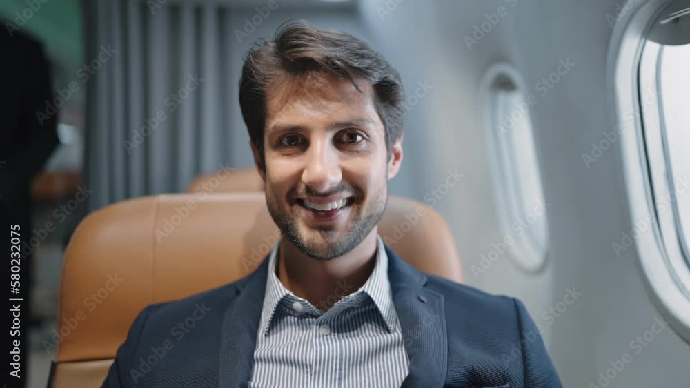 Close up smiling face of Indian businessman wearing suit sitting on seat in airplane looking at camera Close up smiling face of Indian businessman wearing suit sitting on seat in airplane looking at camera