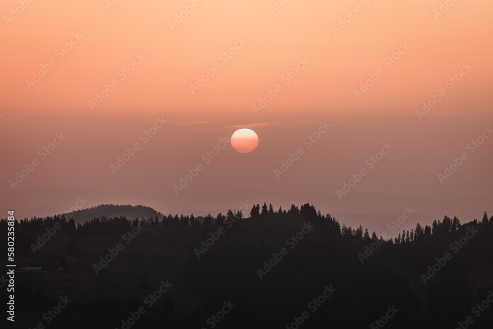 Sonnenglanz im Abendrot: Silhouettenhügel und die strahlende Sonne im Sonnenuntergang Sonnenglanz im Abendrot: Silhouettenhügel und die strahlende Sonne im Sonnenuntergang