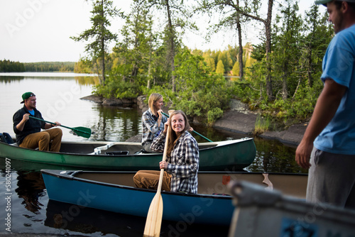 Man looking at friends canoeing on lake against trees
