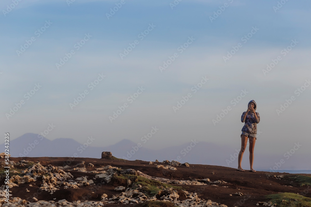 Woman using mobile phone while standing at beach against sky during sunset Woman using mobile phone while standing at beach against sky during sunset
