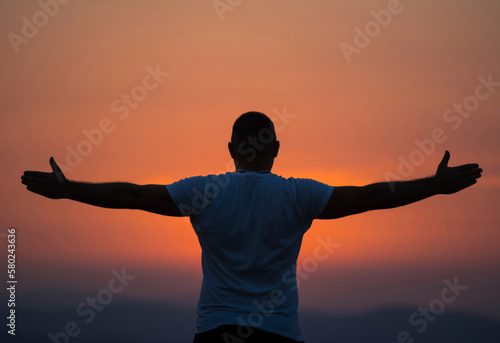 Rear view of carefree man with arms outstretched standing against sky during sunset